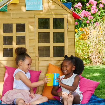  Kids sitting in the garden next to wooden playhouse 